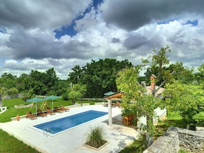 A rectangular swimming pool with lounge chairs and umbrellas, surrounded by a stone wall and lush greenery. - Holiday Home in Rojnici With Private Pool (Barban)