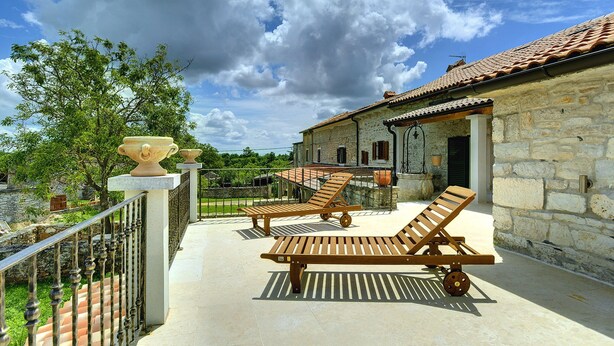 A stone building with a tiled roof, a balcony with two wooden lounge chairs, and a wrought iron fence. - Holiday Home in Rojnici With Private Pool (Barban)