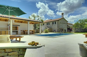 Een stenen huis met een zwembad, terras en een pergola.