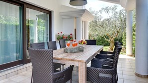A dining area with a large table, wicker chairs, a hanging light fixture, and a view of the garden. - Villa in Medulin With Garden, Private Pool and Sauna Near the Center (Medulin)