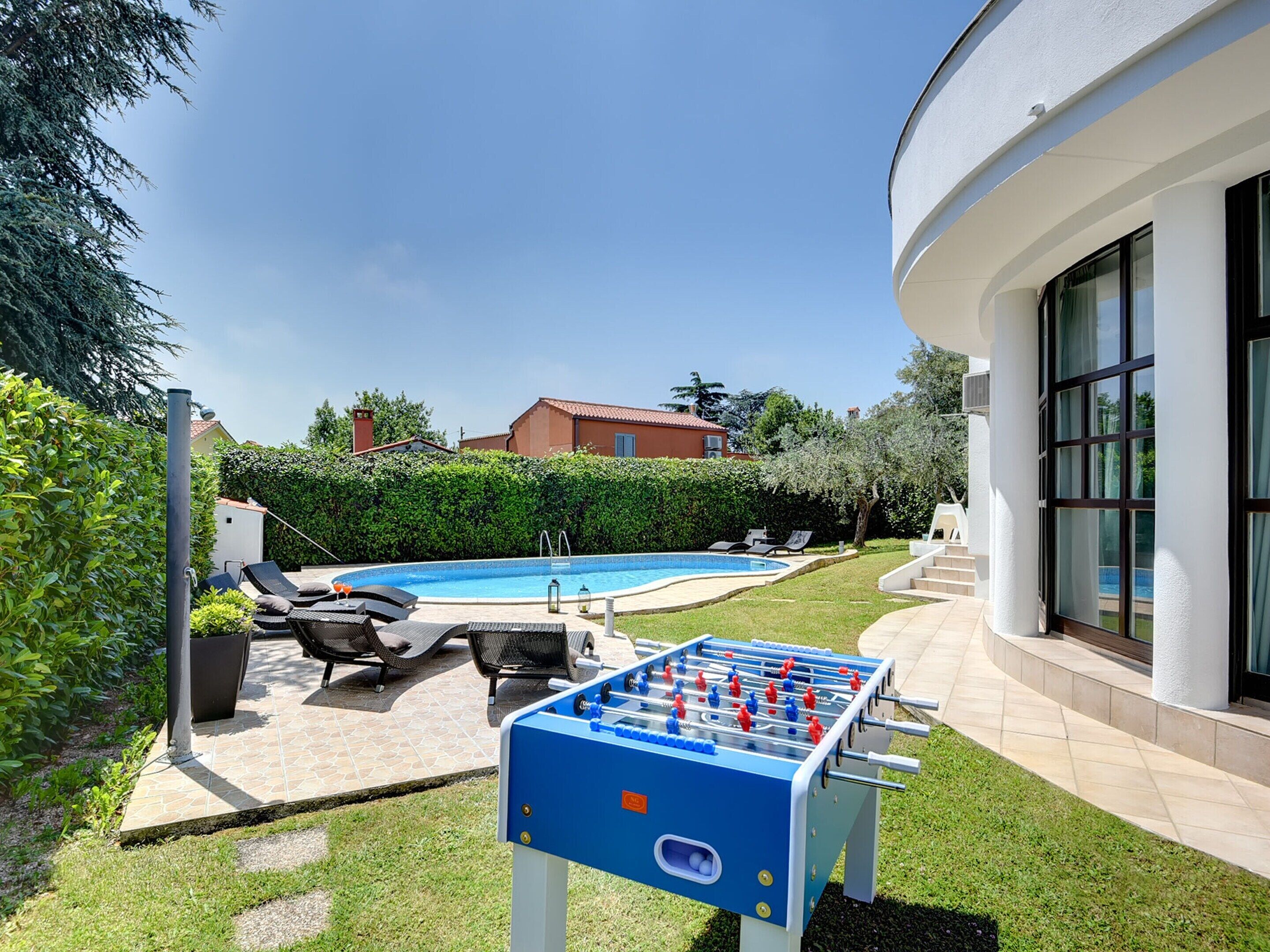 A pool area with a foosball table, lounge chairs, and a clear blue sky.