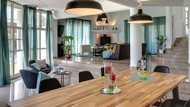 A spacious living area with a wooden dining table, modern pendant lights, and a staircase leading to an upper floor. - Villa in Medulin With Garden, Private Pool and Sauna Near the Center (Medulin)