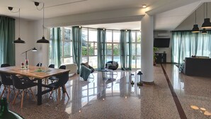 A spacious room with a polished floor, a dining area with a table and chairs, a seating area with a sofa and armchairs, and large windows with curtains. - Villa in Medulin With Garden, Private Pool and Sauna Near the Center (Medulin)
