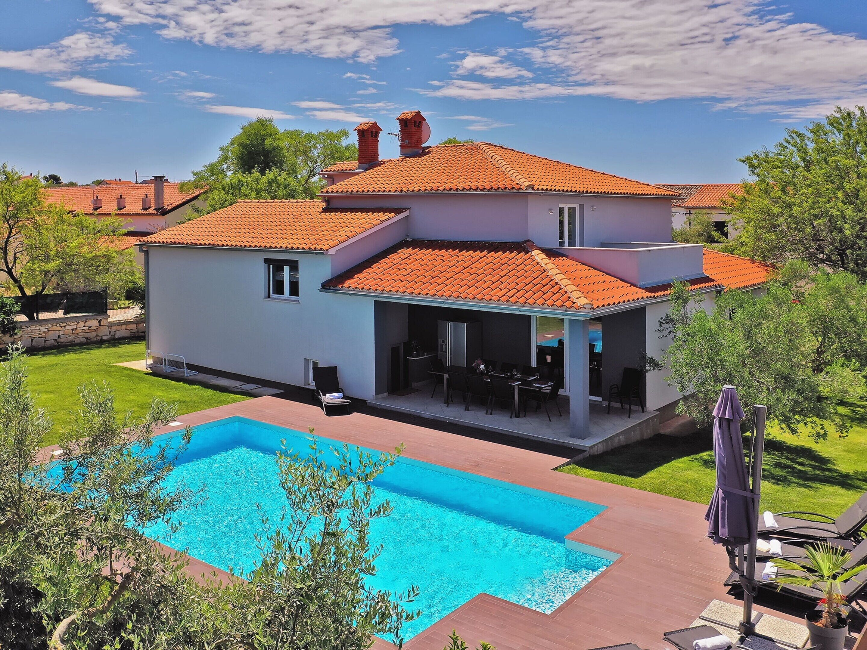 A two-story house with a swimming pool, outdoor seating, and a garden.