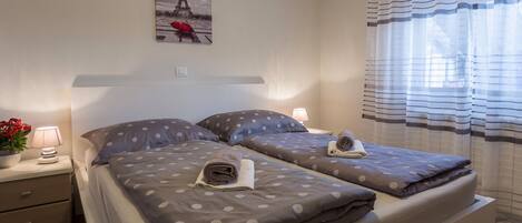 Habitación de hotel con dos camas, una mesita de noche con lámpara, un cuadro de la Torre Eiffel y una ventana con cortinas a rayas.