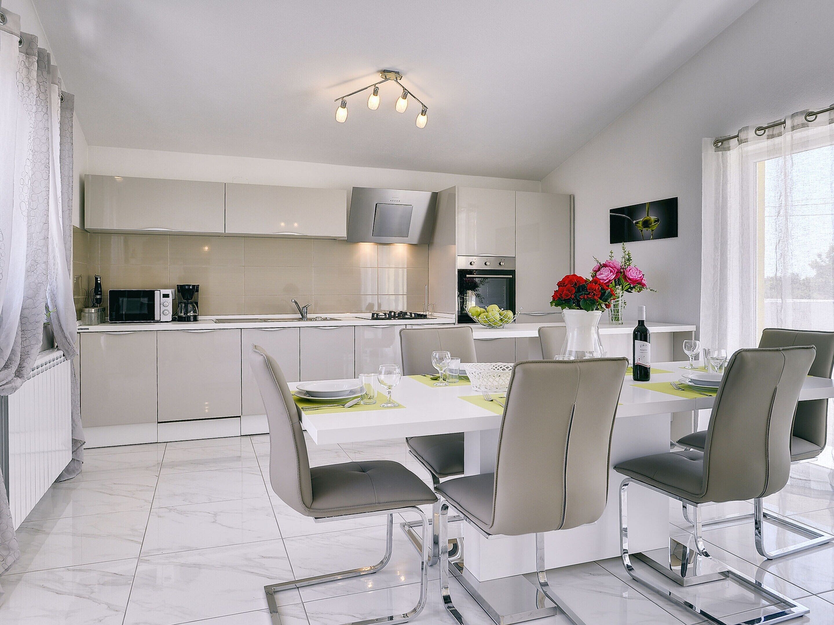 A modern kitchen with white cabinets, a dining area with a white table and chairs, and a kitchen island with a sink and a microwave.