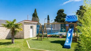 Ein Garten mit einem Steinhaus, einer Schaukel, einer Rutsche und einem umzäunten Spielbereich.