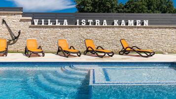 A swimming pool with lounge chairs and a stone wall with the text "VILLA ISTRA KAMEN".