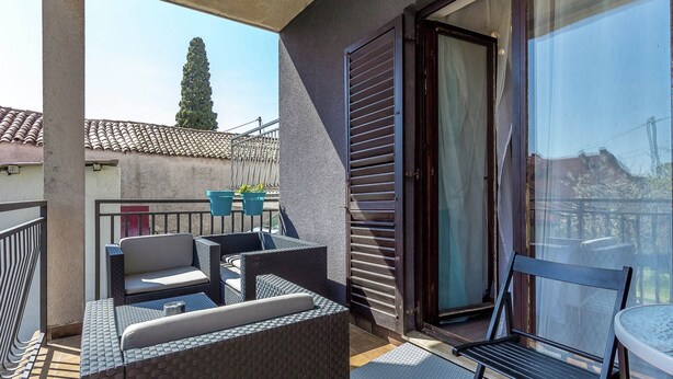 Un balcon agrémenté de meubles en osier, d’une porte vitrée et de plantes en pot.