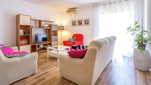Un salon avec un canapé, un fauteuil, une télévision, une bibliothèque et une chaise rouge.