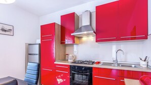 Une cuisine de taille réduite avec des meubles de rangement rouges, une cuisinière, un évier et une machine à café.