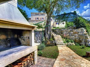 A stone barbecue area with a stone wall and a staircase leading to a building.