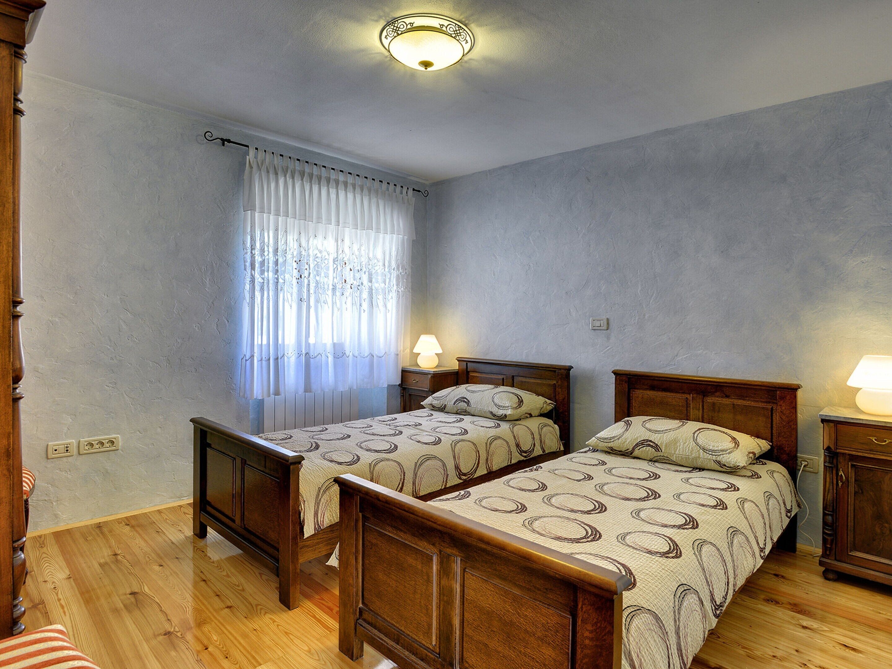 A bedroom with two wooden beds, a window with curtains, and a ceiling light fixture.