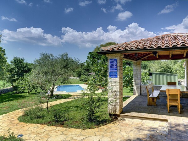 A stone patio with a pool, a covered seating area, and a sign indicating a swimming pool.