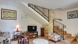 Una sala de estar con una escalera de piedra, un televisor, una mesa de centro y un sofá.