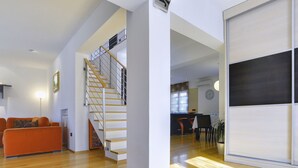 A modern living room with a wooden staircase, a dining area with a bar, and a kitchen in the background. - Modern Holiday Home With Swimming Pool, Terrace With Bbq, Near the Center of Pula (Pula)