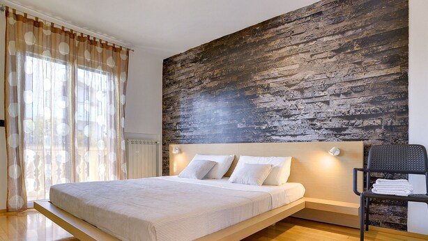 A modern bedroom with a floating bed, a large textured wall, and a chair with towels. - Modern Holiday Home With Swimming Pool, Terrace With Bbq, Near the Center of Pula (Pula)