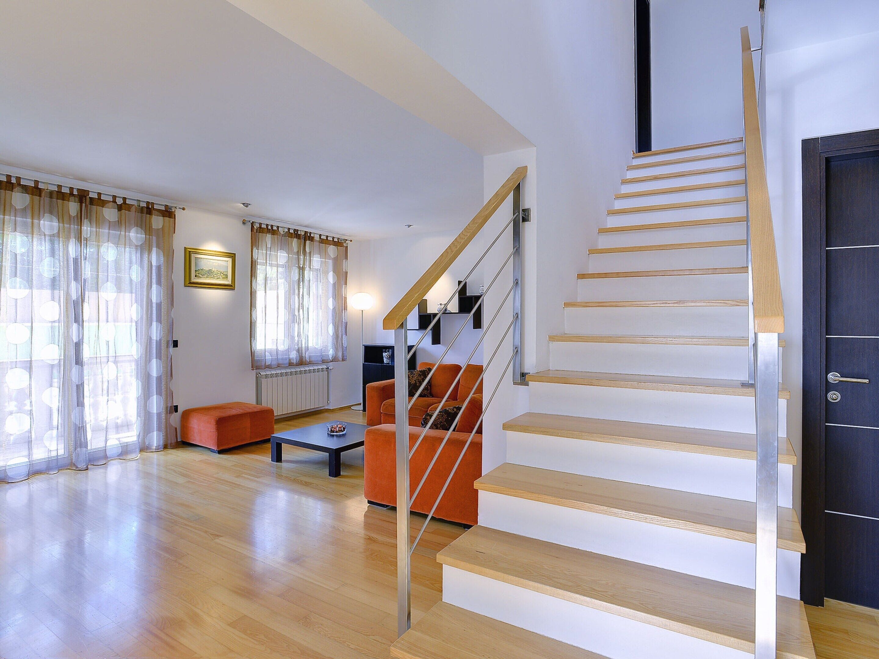A modern living room with a wooden staircase, a sofa, a coffee table, and a radiator.