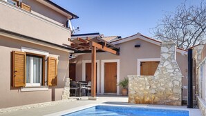 A swimming pool with a stone wall and wooden shutters, surrounded by a building with a pergola and a door. - Modern Holiday Home With Swimming Pool, Terrace With Bbq, Near the Center of Pula (Pula)
