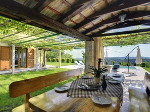 An outdoor patio with a wooden table set for dining, a bench, and a view of a swimming pool and mountains in the background.
