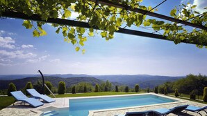 A swimming pool with stone tiles, surrounded by lounge chairs, and a view of distant mountains. - Villa in Lupoglav With Pool Near the Sea (Lupoglav)