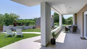 Un espace extérieur abrité, doté d’une terrasse, de sièges et d’une plante en pot.