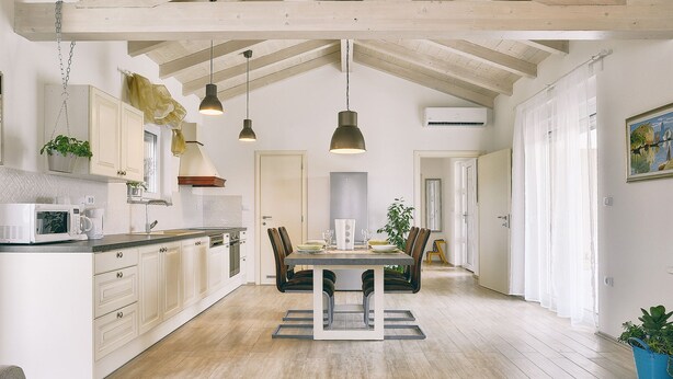 Une cuisine spacieuse avec des poutres en bois, un coin repas avec une table et des chaises, et une vue sur le salon.
