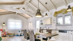 Une cuisine spacieuse avec des poutres en bois, un coin repas avec une table et des chaises, et une fenêtre qui laisse entrer la lumière naturelle.