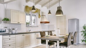 Une cuisine moderne avec des meubles blancs, une table à manger avec des chaises, des luminaires suspendus et un réfrigérateur.