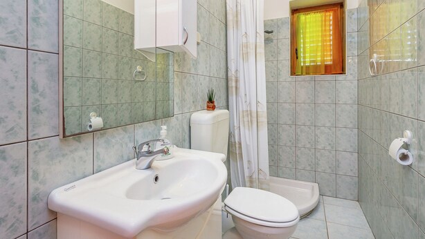 Baño con lavamanos, inodoro y zona de ducha blancos.
