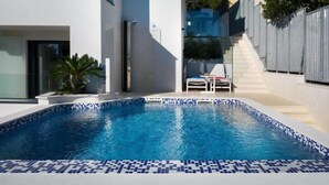 A modern swimming pool with a tiled edge, a lounge chair, and a staircase leading to a balcony. - Villa in Pula With Private Swimming Pool (Medulin)