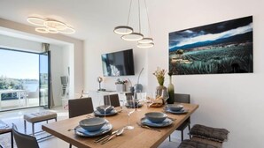 A modern dining area with a wooden table set for four, a large flat-screen TV on the wall, and a scenic landscape painting above the table. - Villa in Pula With Private Swimming Pool (Medulin)