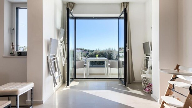 A modern room with a balcony, a table with chairs, and a view of the city. - Villa in Pula With Private Swimming Pool (Medulin)