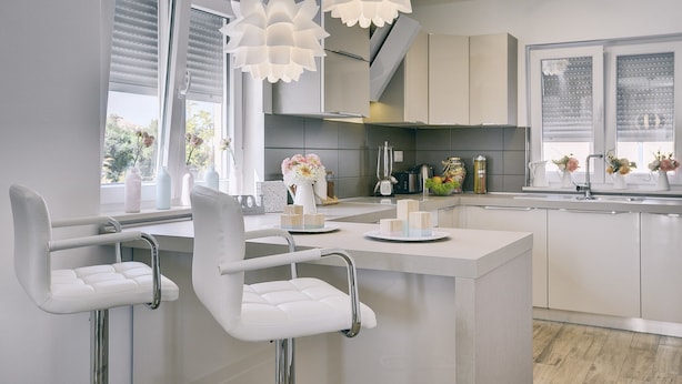 Una cocina moderna con taburetes blancos, una isla central e iluminación colgante.