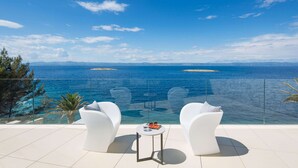 A terrace with two white chairs and a small table, overlooking a clear blue sea with distant islands. - Beach Villa in Korcula with Pool, Sauna & Hot Tub (Blato)