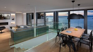 A modern living space with a glass railing, a dining area with a wooden table and chairs, and a view of the sea. - Beach Villa in Korcula with Pool, Sauna & Hot Tub (Blato)