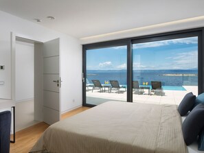 A bedroom with a large bed, a wardrobe, and a sliding glass door leading to a balcony with a pool and chairs. - Beach Villa in Korcula with Pool, Sauna & Hot Tub (Blato)