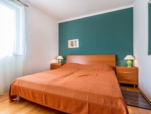 A bedroom with a wooden bed, teal walls, two bedside tables with lamps, and a window with curtains. - Charming Apartment in Pula With Swimming Pool (Liznjan)