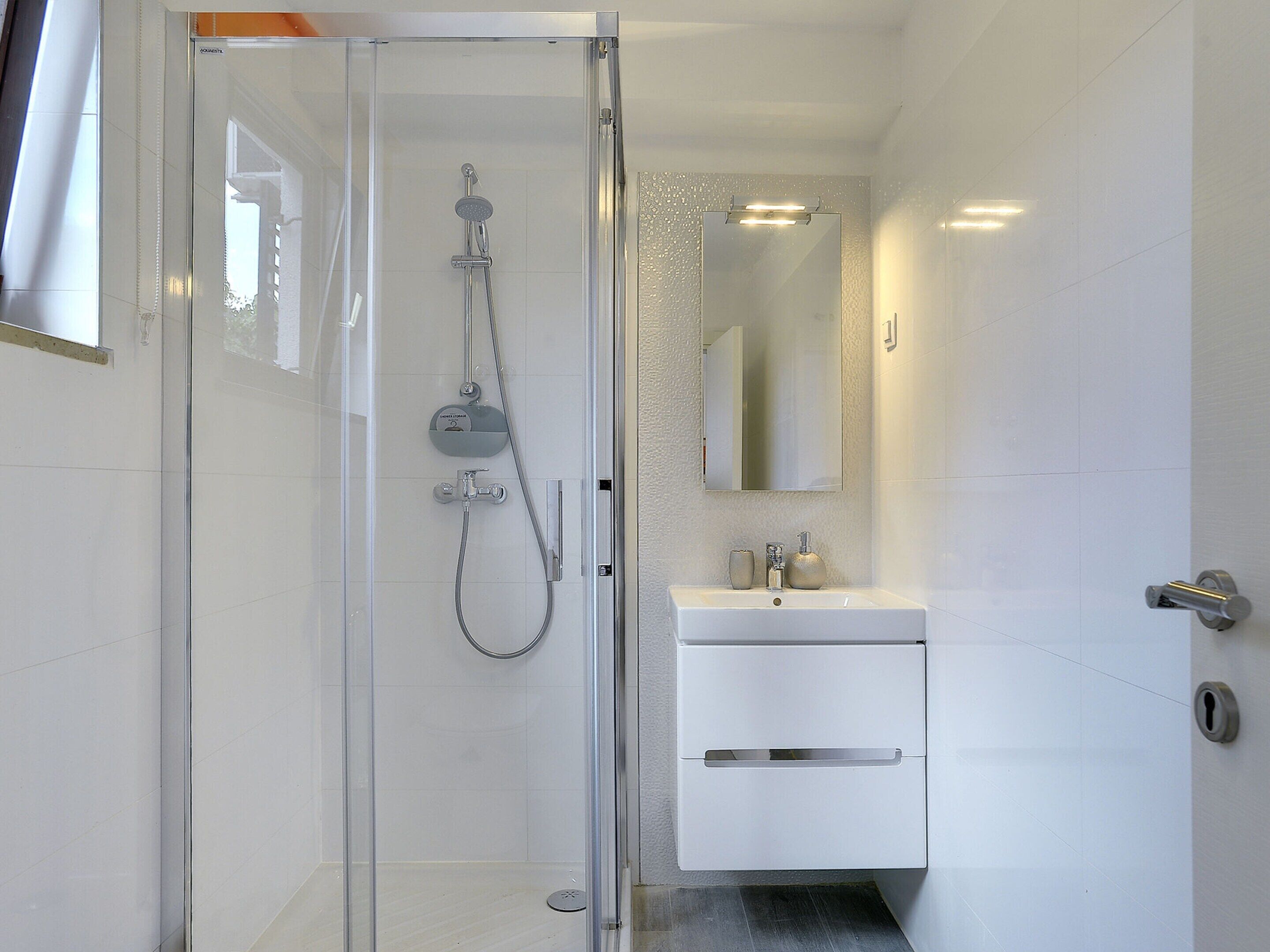 Een moderne badkamer met een douche met glazen wand, een wit wastafelmeubel en een spiegel erboven.