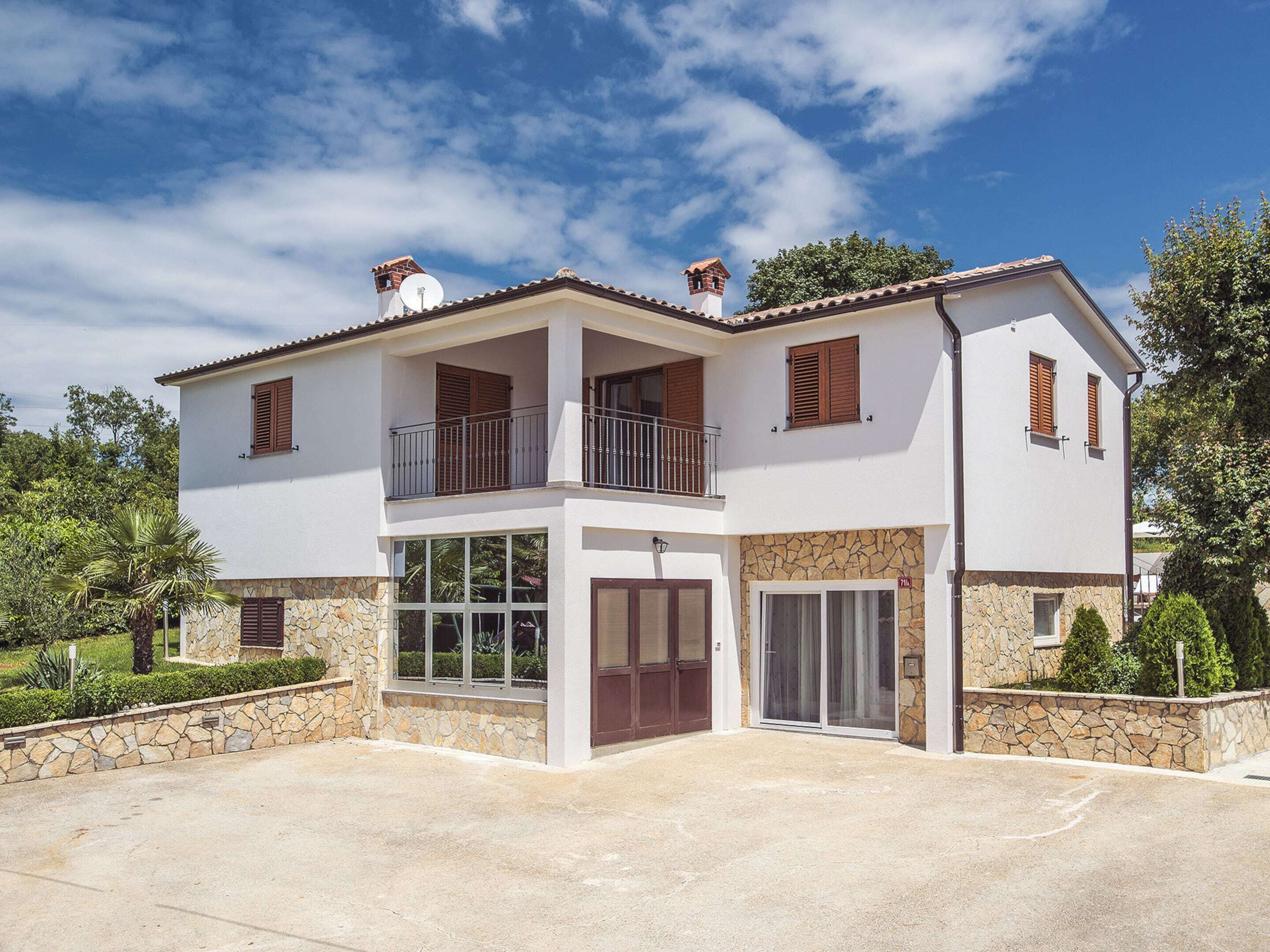 Une maison à deux étages avec une façade en pierre, un balcon et un garage.