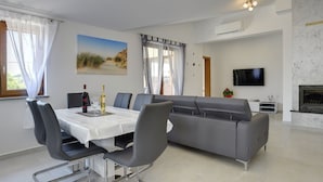 A modern living room with a dining area, a grey sofa, a flat-screen TV, and a fireplace. - Modern Holiday Home With Pool in Pazin (Pazin)