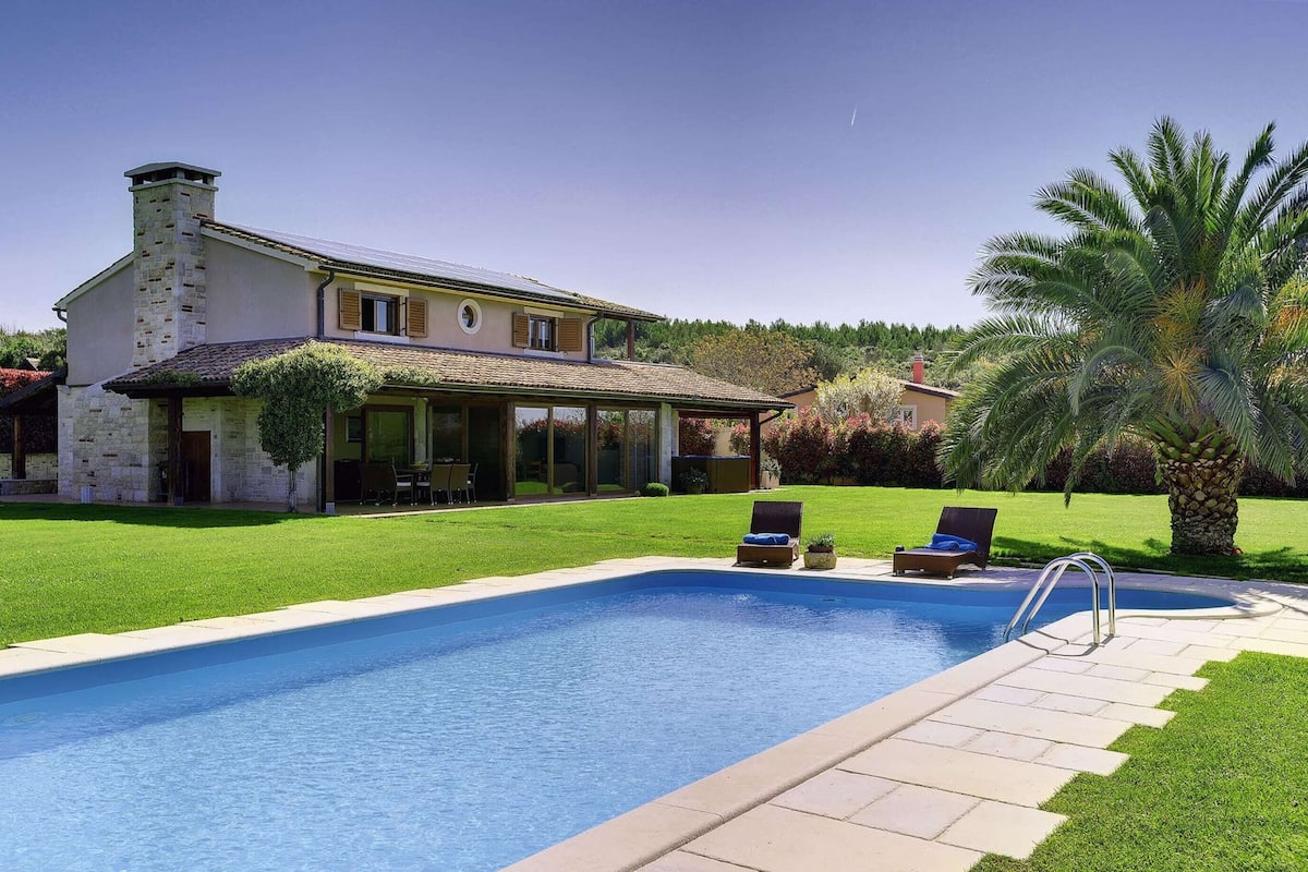 Una casa con piscina, jardín y una palmera.