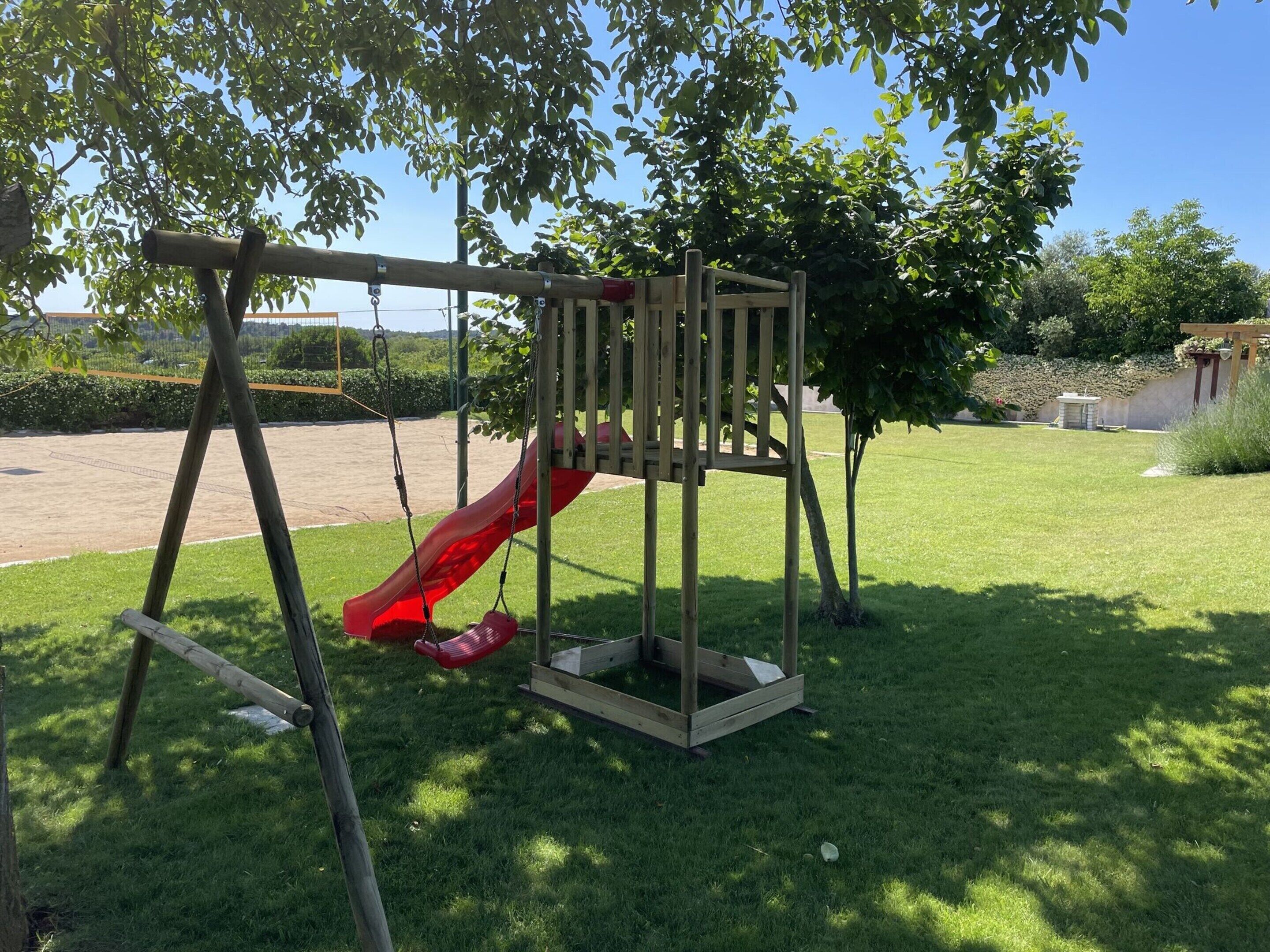 Un parque infantil de madera con un tobogán rojo en un área con césped.