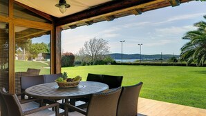 A covered patio with wicker furniture and a table, overlooking a well-maintained lawn and distant hills. - Luxurious Villa in Pomer with Pool & Hot Tub (Medulin)