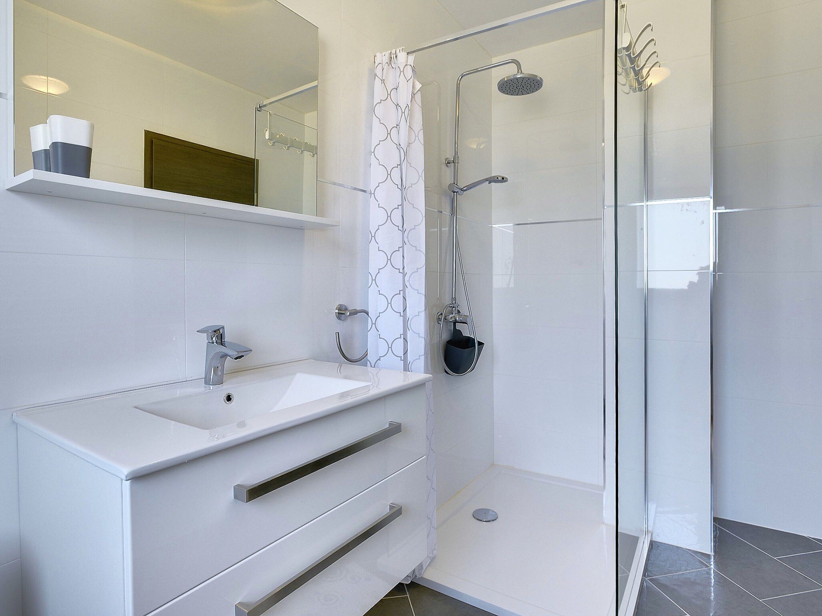 A modern bathroom with a glass shower enclosure, a white sink with a chrome faucet, and a mirror above the sink.