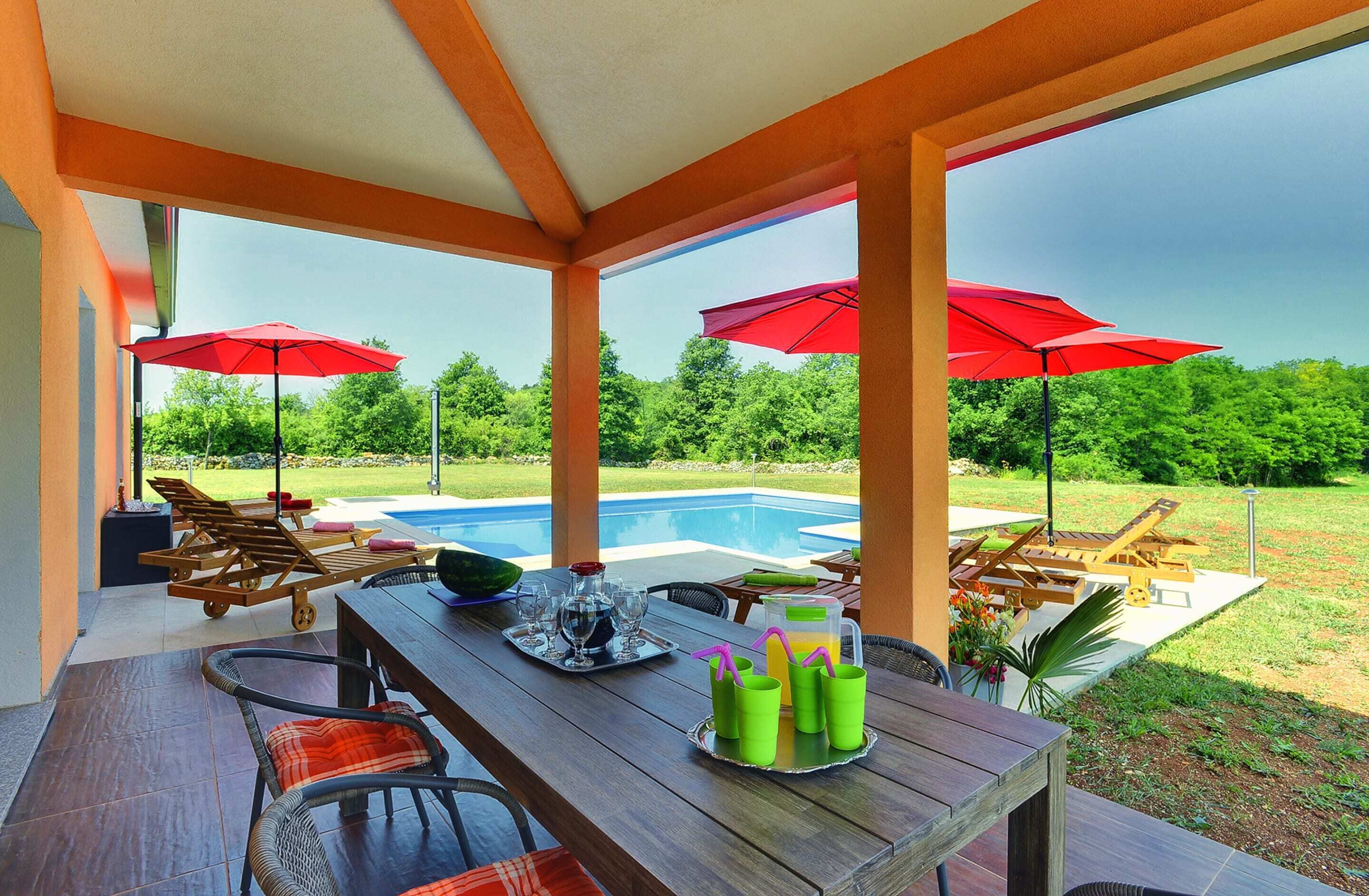 Une terrasse extérieure avec une piscine, des meubles en bois et des parasols rouges.