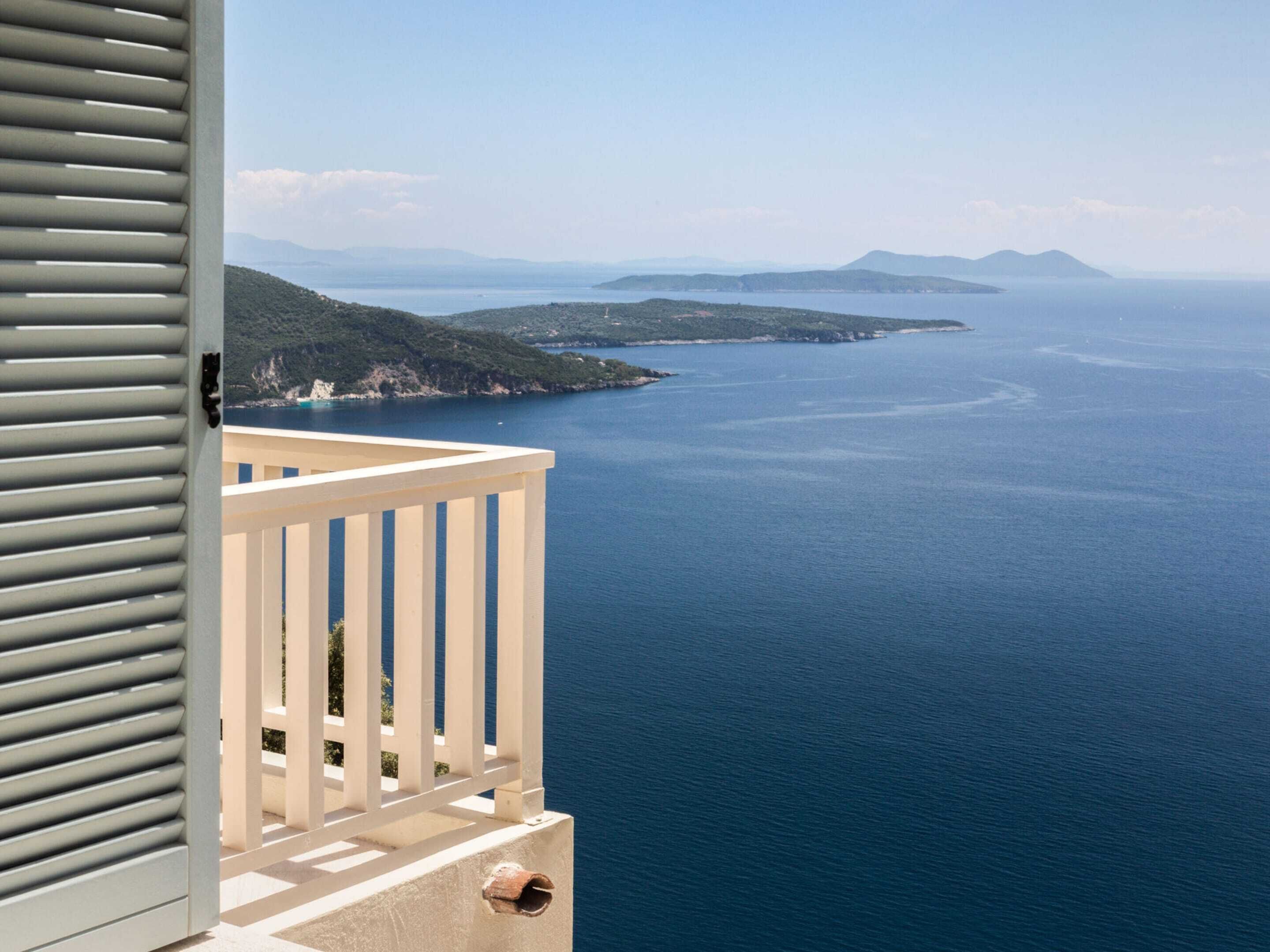 A balcony with a view of a calm sea and distant mountains.