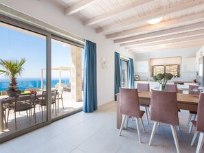 A spacious dining area with a view of the sea, a kitchen with modern appliances, and a balcony with a palm tree. - Scenic Villa With Private Pool (Kissamos)