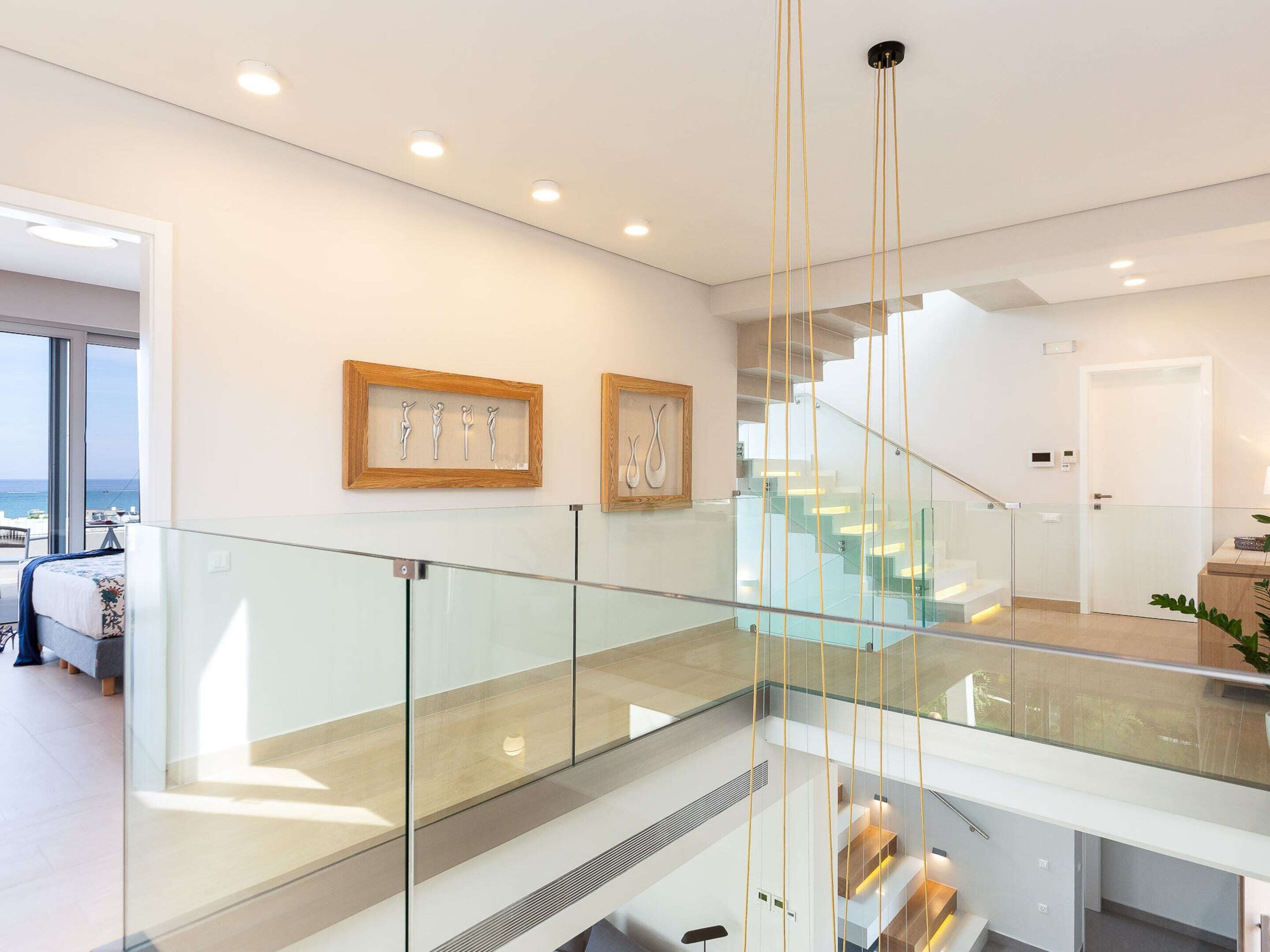 A modern interior with a glass railing, a staircase, and artwork on the walls.