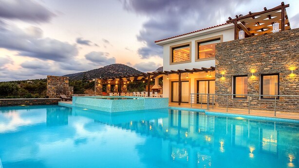 Un espace moderne aménagé au bord de la piscine, avec une eau cristalline, des murs en pierre et une vue sur une montagne.